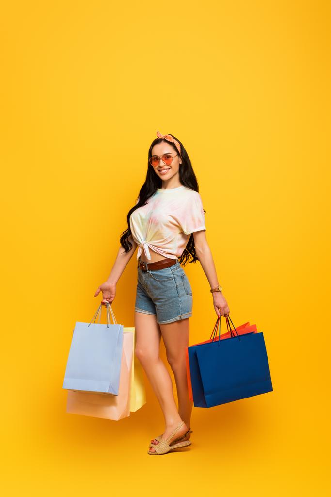 lächelnd stilvolle Sommer Brünette Mädchen mit Einkaufstaschen auf gelbem Hintergrund - Foto, Bild