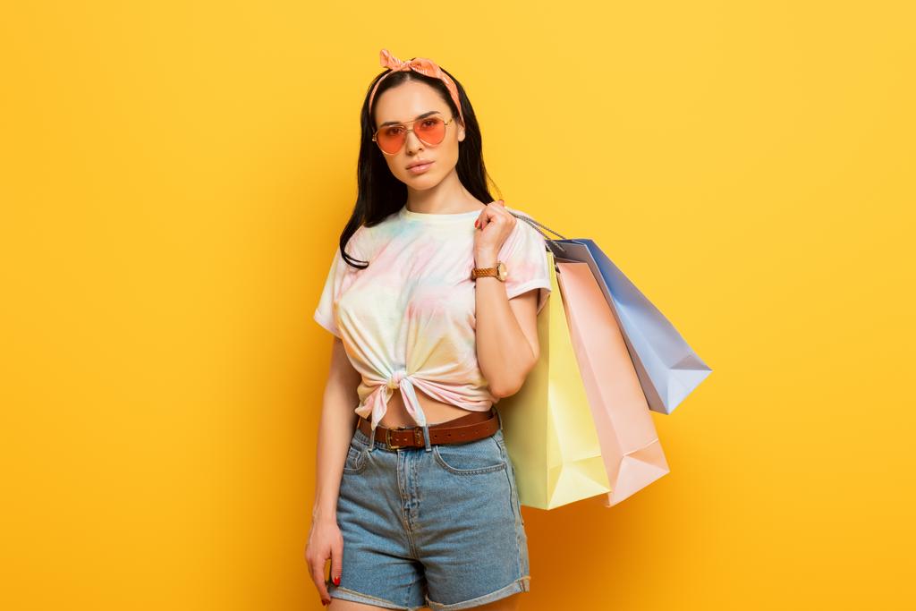 serieuze stijlvolle zomer brunette meisje met boodschappentassen op gele achtergrond - Foto, afbeelding