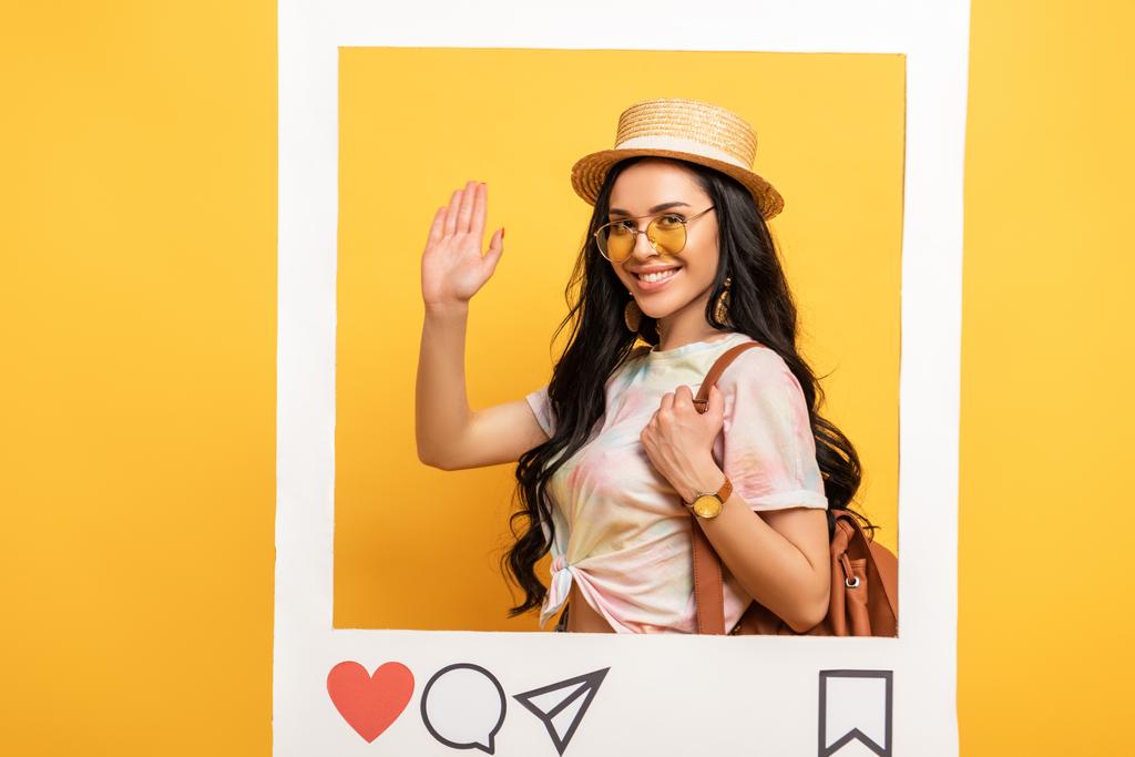 χαρούμενη μελαχρινή κοπέλα με καλοκαιρινή στολή κουνώντας το χέρι στο πλαίσιο του κοινωνικού δικτύου σε κίτρινο φόντο - Φωτογραφία, εικόνα