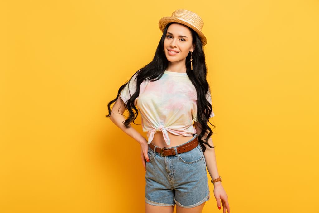 smiling brunette girl in straw hat with hand on hip on yellow background - Photo, Image