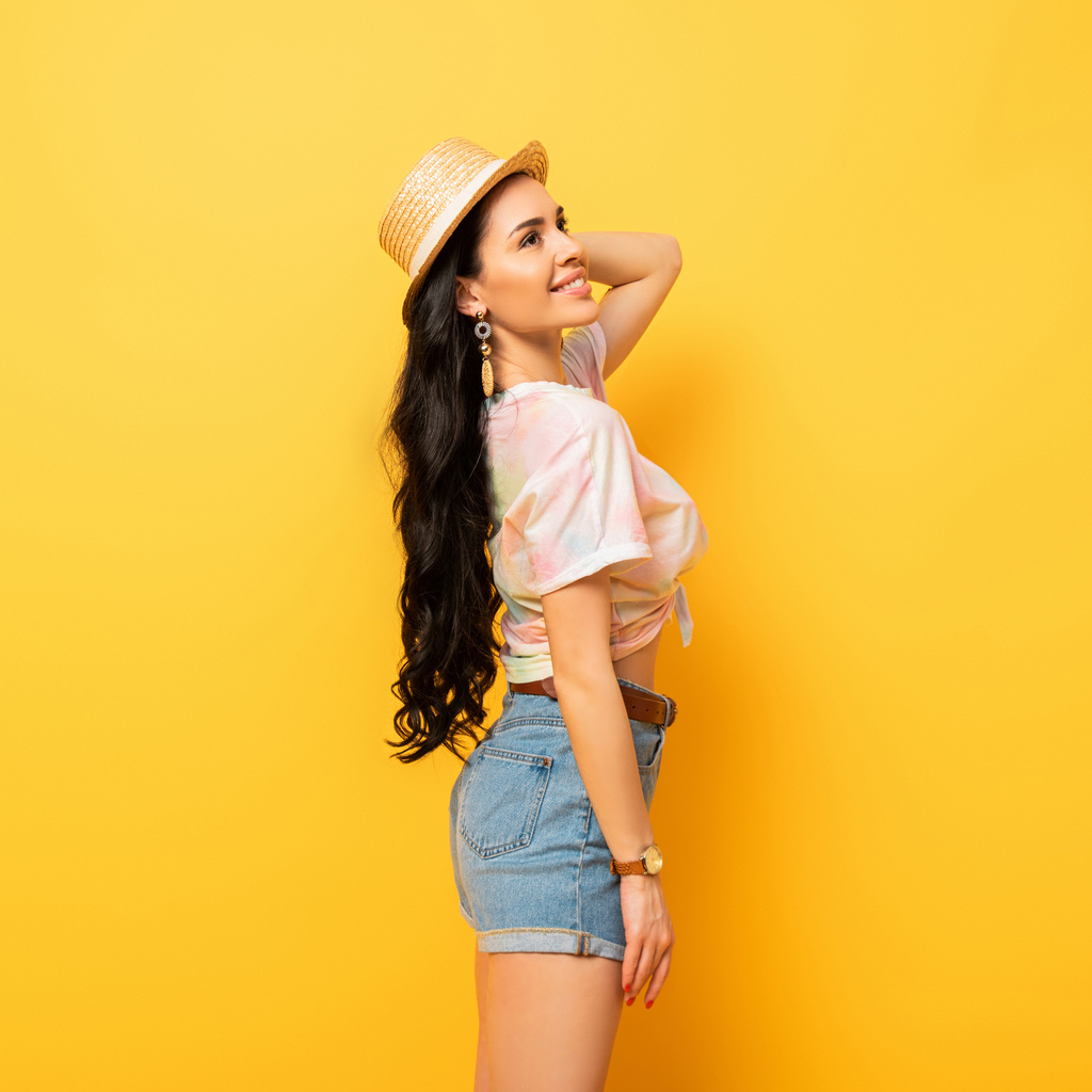side view of smiling brunette girl in straw hat on yellow background - Photo, Image