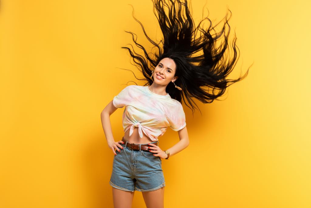 ευτυχισμένη μελαχρινή κοπέλα κουνώντας τα μαλλιά σε κίτρινο φόντο - Φωτογραφία, εικόνα