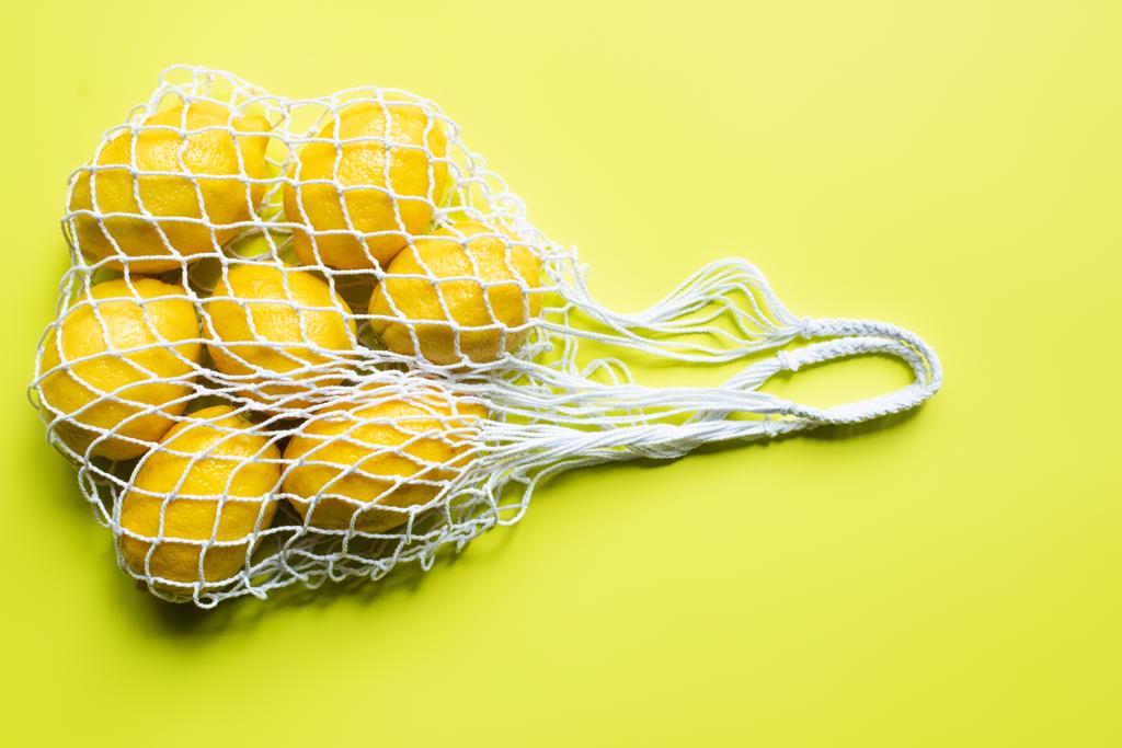 top view of ripe whole lemons in string bag on yellow background - Photo, Image