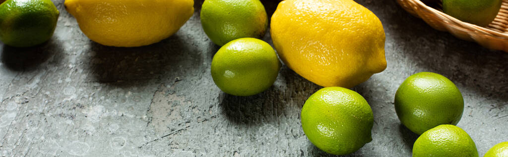Beton desenli yüzeyde olgun sarı limonlar ve yeşil limonlar, panoramik mahsuller. - Fotoğraf, Görsel