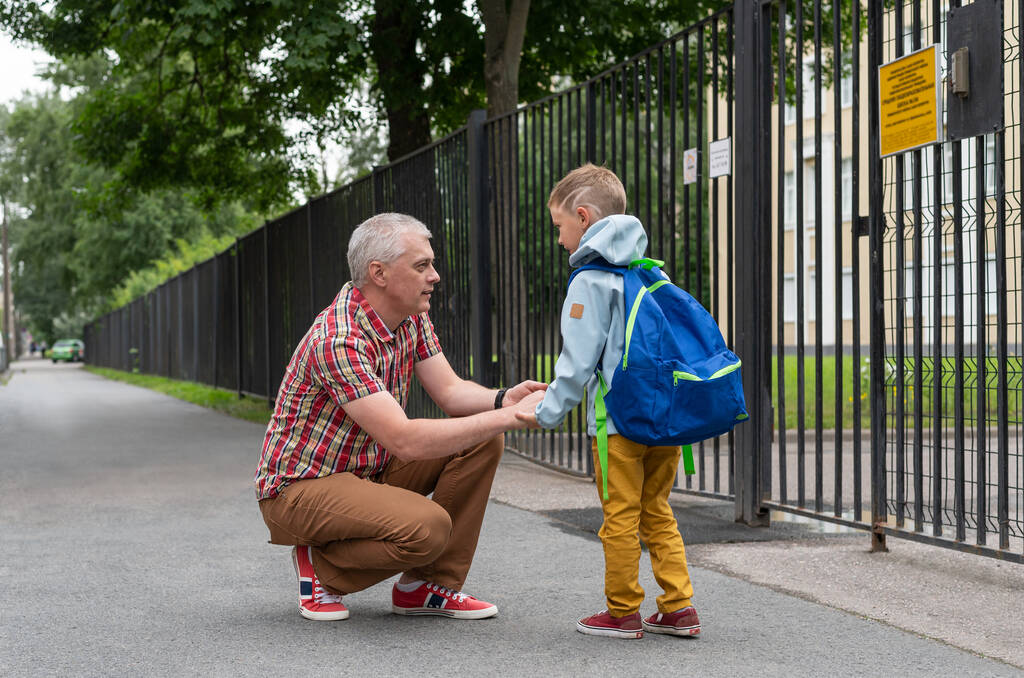 お父さんは学校の近くの息子にさよならを言った。朝学校の近くで話してる父と息子. - 写真・画像