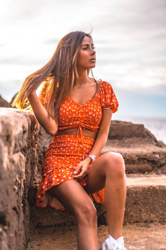 Een jonge brunette Kaukasische vrouw in een rode jurk op het strand van Itzurrun in de stad Zumaia, Gipuzkoa. Baskenland. Lifestyle sessie, genieten van de zee op trappen glimlachend - Foto, afbeelding