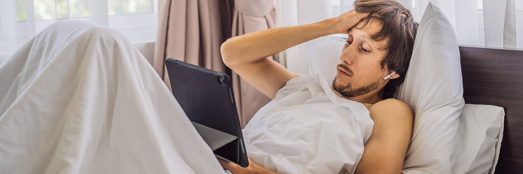 男性患者は彼のベッドに横たわっている間病気であり、ガジェットバナーを介してオンライン医師を呼び出します,ロングフォーマット - 写真・画像