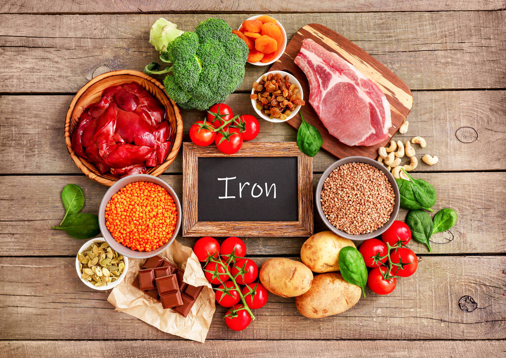 Assortment of high in Iron sources on wooden background: liver, beef, raisins, keshew, buckwheat, spinach, tomatoes, potatoes, dark chocolate, pumpkin seeds, lentil, broccoli, dried appricots. Top view. - Photo, Image
