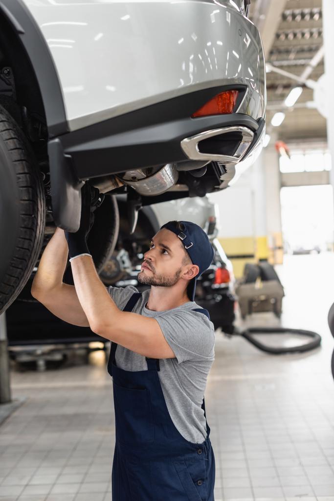 selective focus of handsome mechanic in uniform and cap fixing car  - Photo, Image