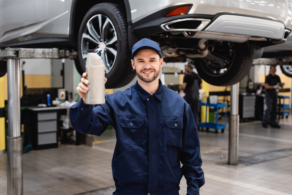 selektivní zaměření veselého mechanika v uzávěru drží láhev s automobilovým olejem  - Fotografie, Obrázek