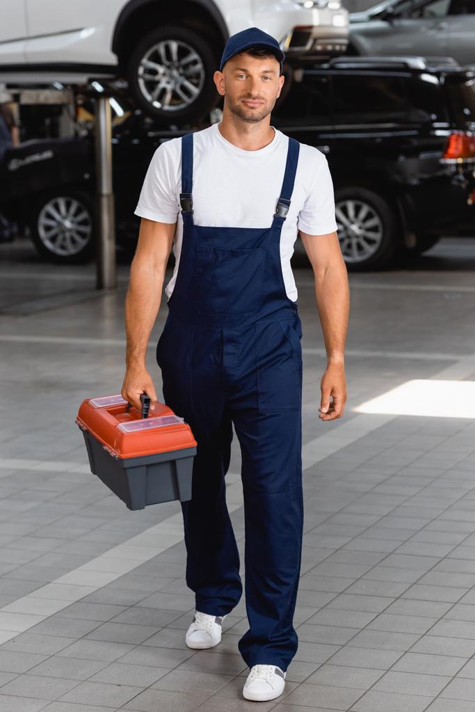schöner Mechaniker in Uniform und Mütze mit Werkzeugkiste in der Tankstelle - Foto, Bild