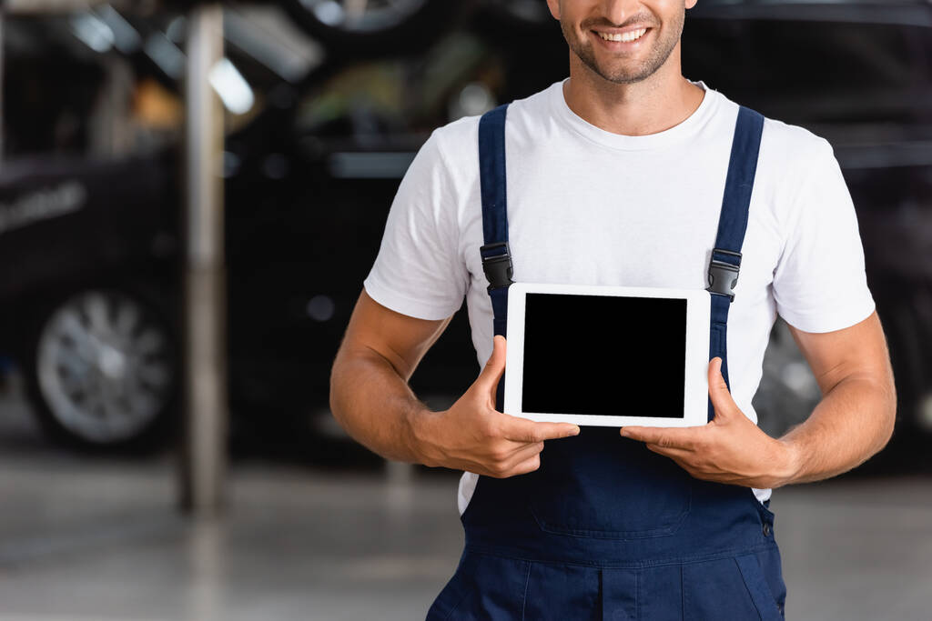 rajattu näkymä onnellinen mekaanikko haalarit tilalla digitaalinen tabletti tyhjä näyttö auton palvelun  - Valokuva, kuva