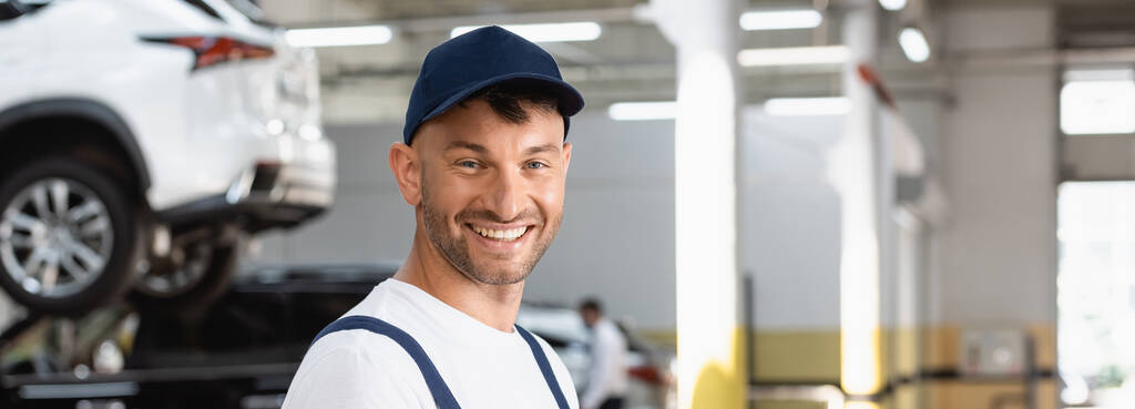 Panoramaaufnahme eines glücklichen Mechanikers mit Mütze, der in die Kamera blickt - Foto, Bild