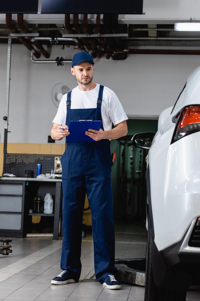 mechanic in uniform holding clipboard while looking at car - Photo, Image