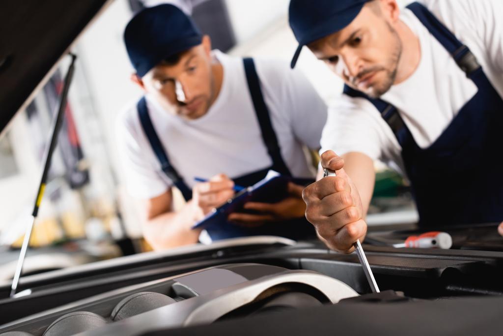 selective focus of mechanic in cap repairing car near coworker with clipboard and pen  - Photo, Image