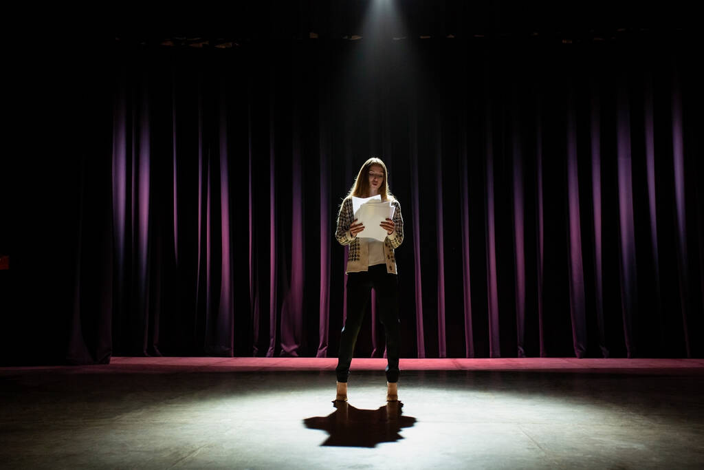 Una giovane attrice che prova il suo discorso sul palco. Scena buia con illuminazione drammatica - Foto, immagini