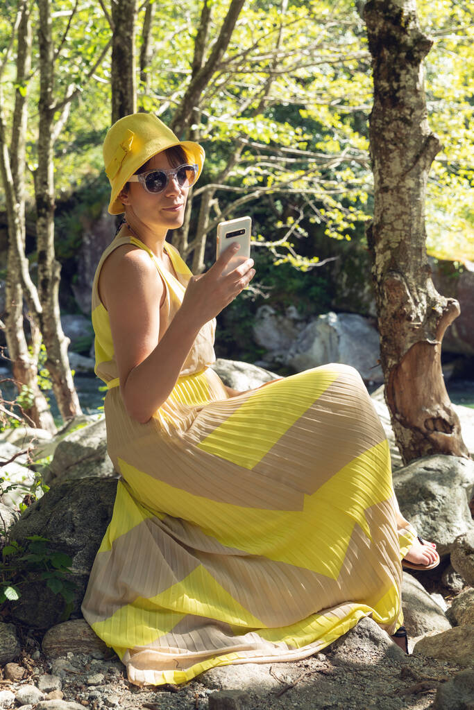 Krásná žena sedí v lese se žlutými šaty a telefonem - Fotografie, Obrázek