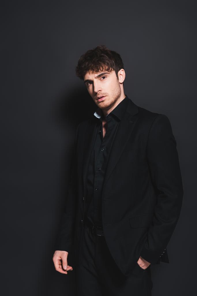 красивий чоловік у формальному одязі стоїть з рукою в кишені на чорному
  - Фото, зображення