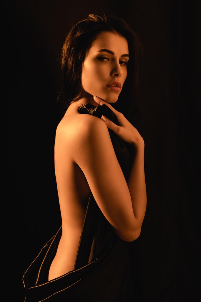 donna sensuale e nuda coperta da lenzuolo di seta isolato su nero  - Foto, immagini