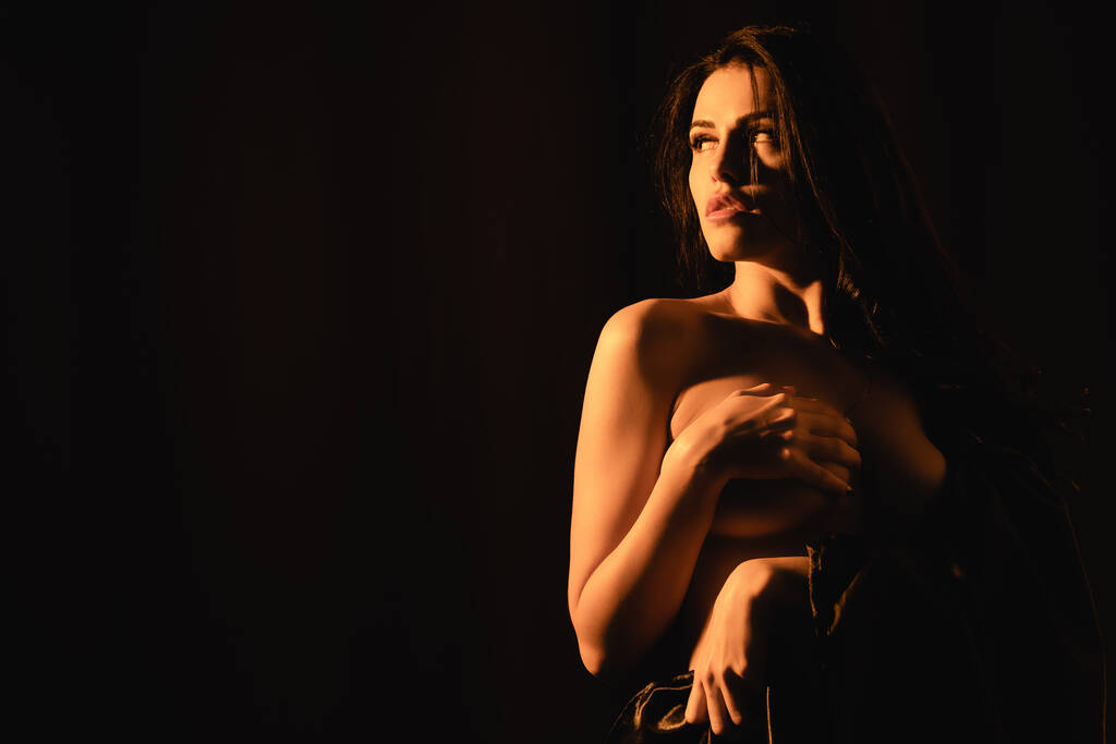 Beleuchtung der attraktiven Frau in seidenes Bettlaken gehüllt, Brust isoliert auf schwarz  - Foto, Bild