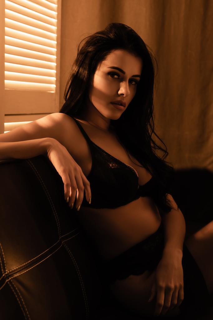 σέξι γυναίκα με δαντελωτά εσώρουχα κάθεται σε μαύρο καναπέ - Φωτογραφία, εικόνα