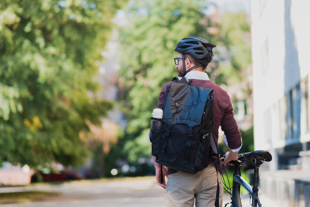 Мужчина пригородный или курьер с велосипедом в городском фоне. Безопасная езда на велосипеде по городу, езда на работу на велосипеде, изображение курьера - Фото, изображение