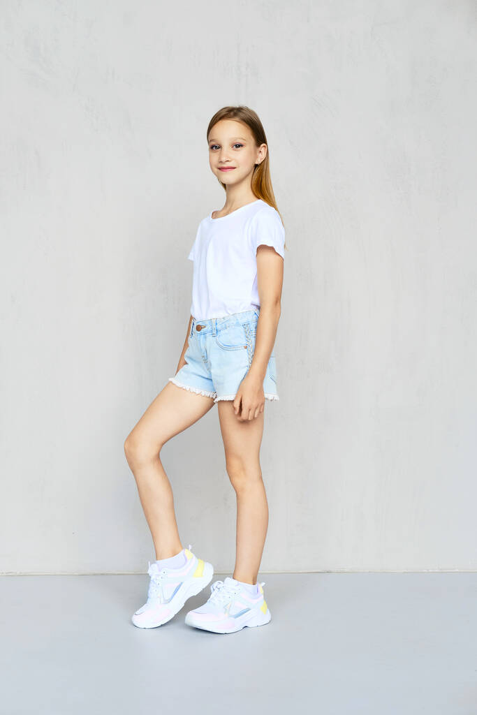 Молодая спортивная девушка в белой футболке и джинсовых шортах позирует в студии
 - Фото, изображение
