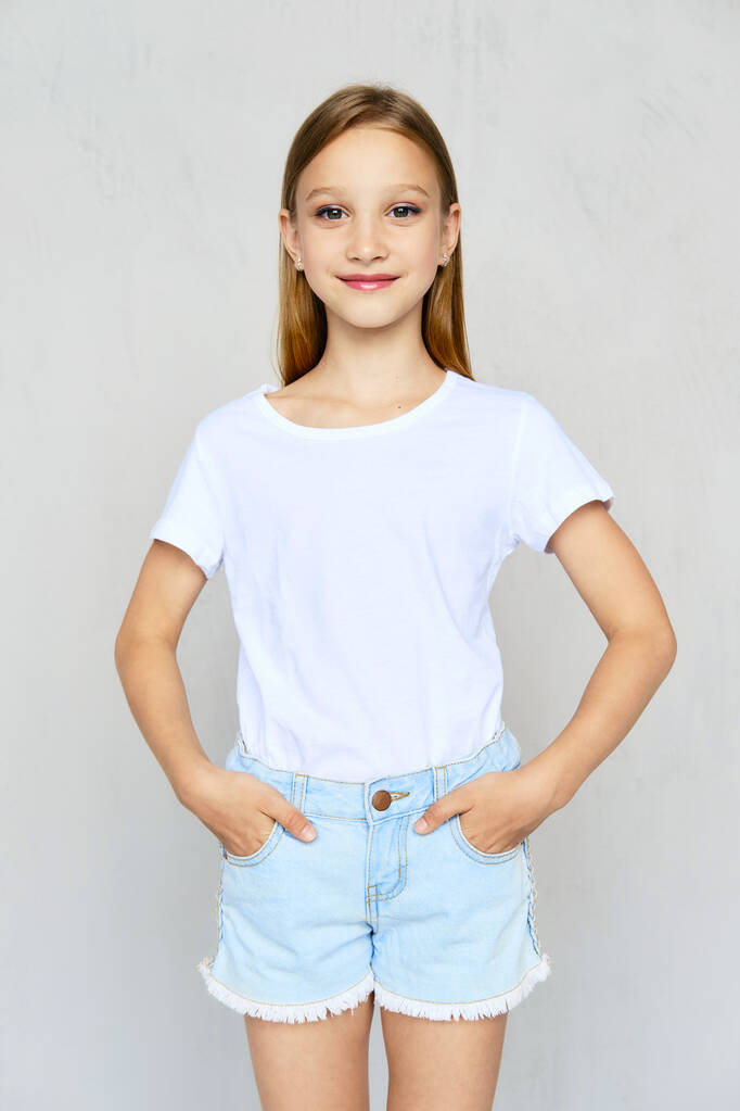 Jeune fille sportive en t-shirt blanc avec les mains en poskets de jeans short posant en studio - Photo, image