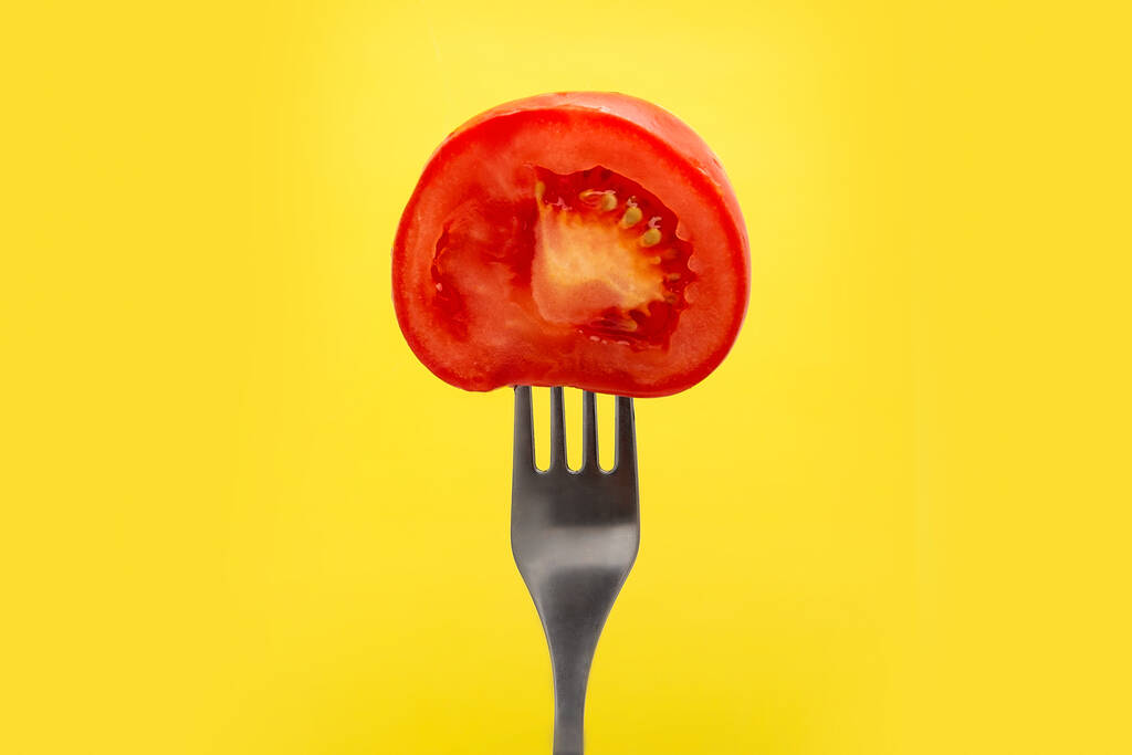 Meio tomate fresco vermelho em um garfo em um fundo amarelo
 - Foto, Imagem
