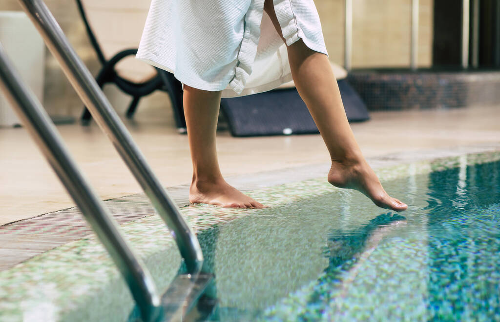 Zdjęcie kobiecych nóg, gdy próbuje wody w hotelowym basenie. Wakacje i rekreacja w spa - Zdjęcie, obraz
