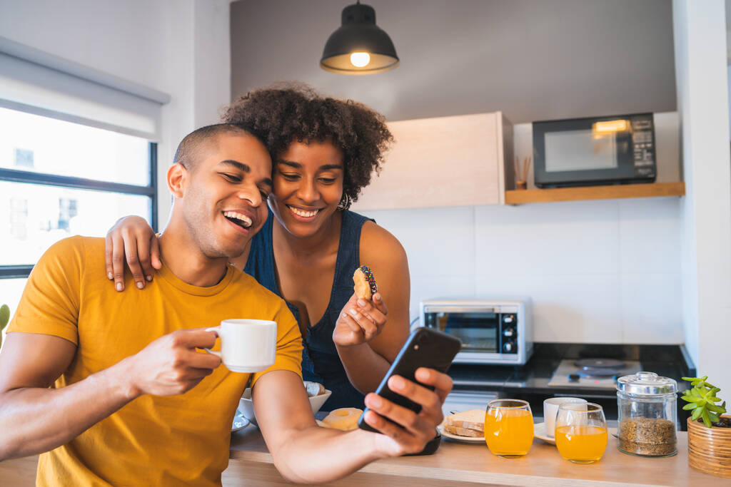 Portret van een gelukkig jong stel dat een selfie maakt met een mobiele telefoon terwijl ze samen ontbijten thuis. Relatie en leefstijlconcept. - Foto, afbeelding