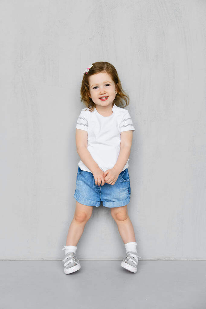 Beyaz tişörtlü, kot şortlu, stüdyoda poz veren iki yaşında bir kız. - Fotoğraf, Görsel