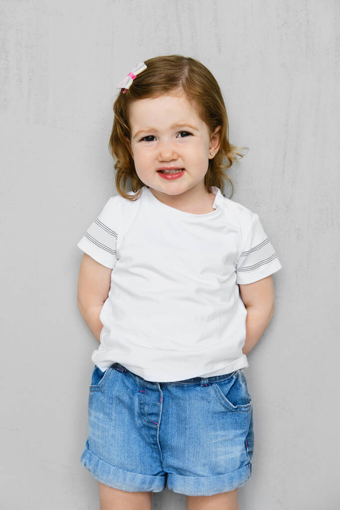 Fille de deux ans en t-short blanc et short en jeans posant en studio - Photo, image