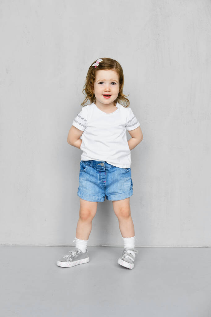 Dois anos de idade menina em t-short branco e calções de ganga posando em estúdio
 - Foto, Imagem