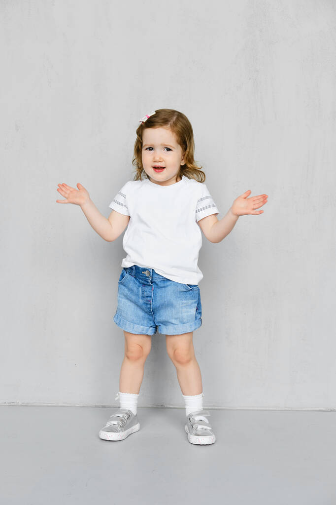 Chica de dos años en pantalones cortos blancos y pantalones vaqueros posando en el estudio
 - Foto, Imagen