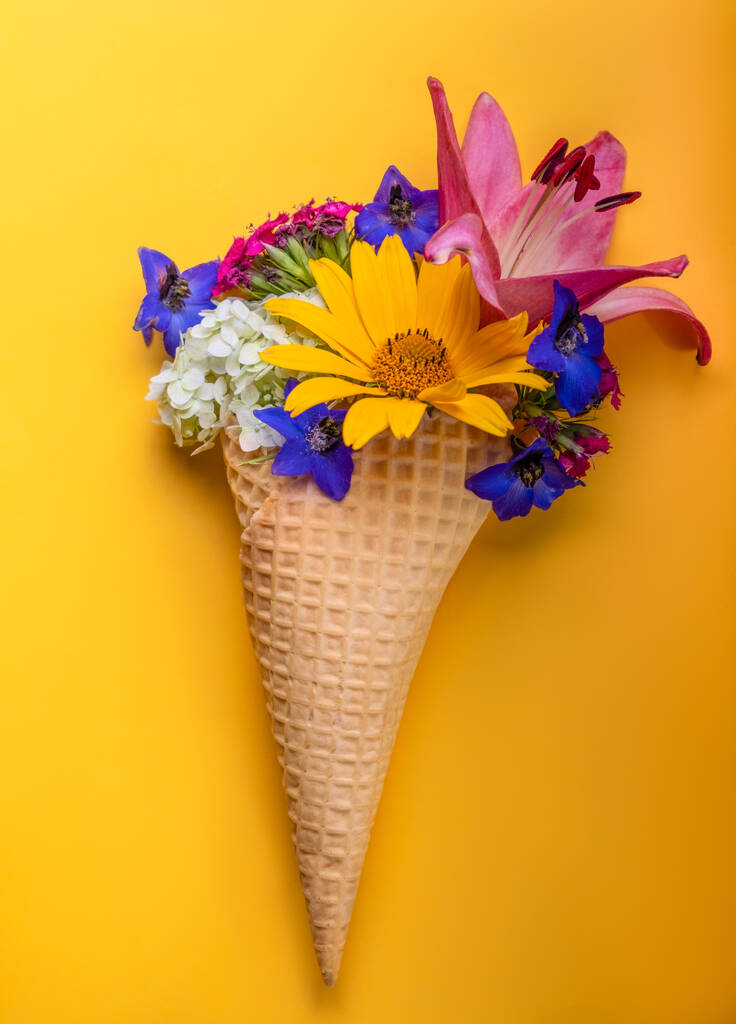 Waffle cone with spring flowers, vanilla style on a yellow background. - Photo, Image