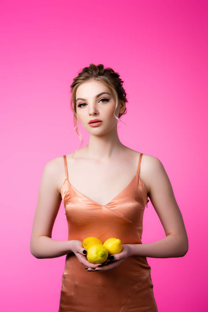 élégante belle femme blonde tenant citrons mûrs isolés sur rose - Photo, image