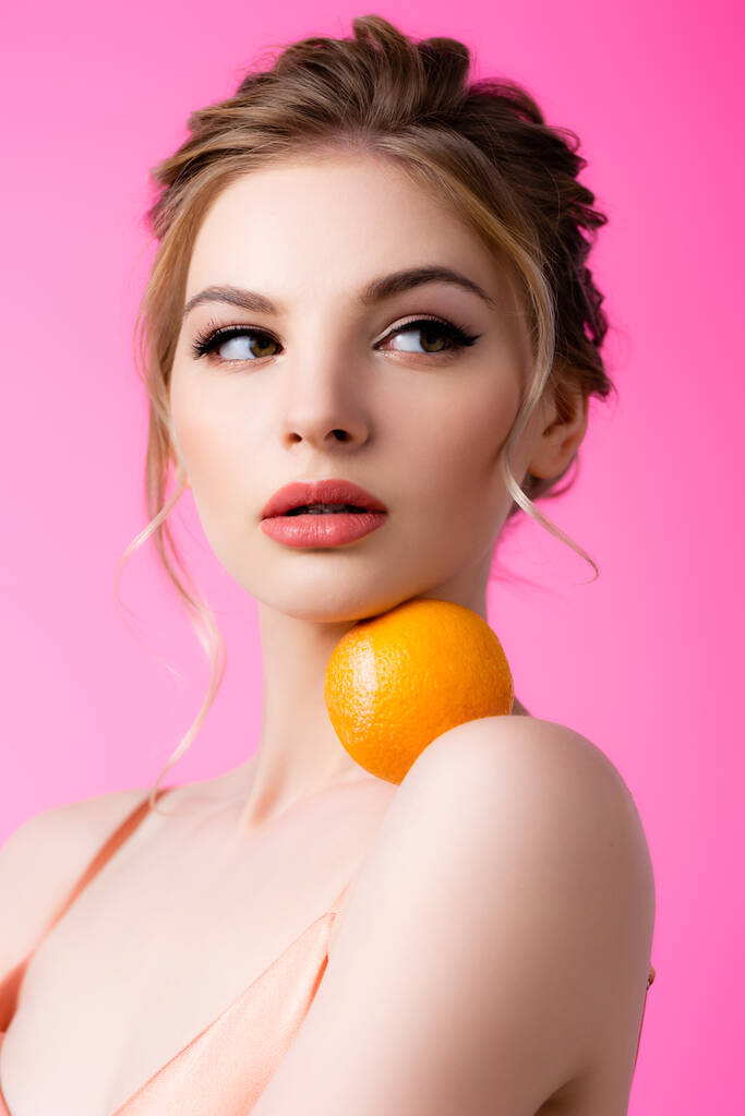 elegáns gyönyörű szőke nő gazdaság érett narancs vállán elszigetelt rózsaszín - Fotó, kép