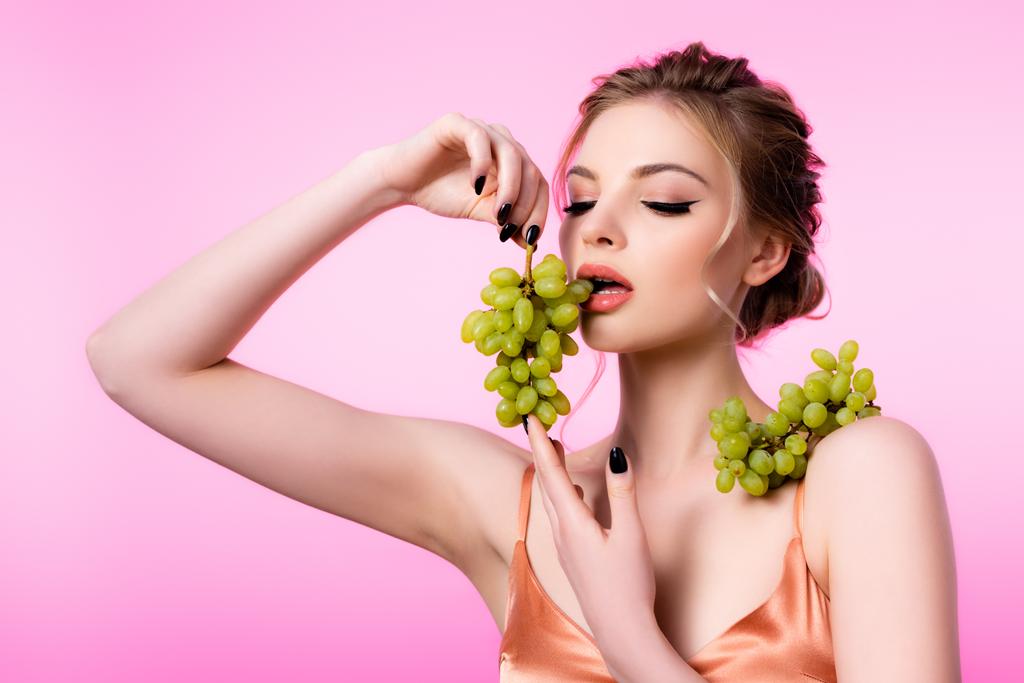 elegant beautiful blonde woman eating green grapes isolated on pink - Photo, Image