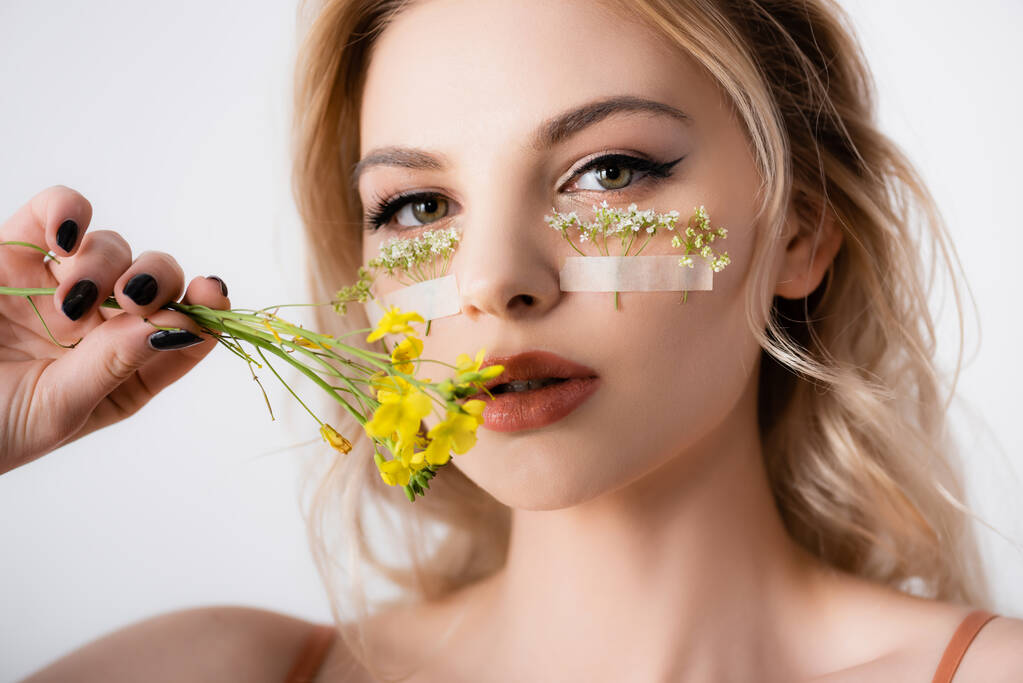 hermosa mujer rubia con flores silvestres bajo los ojos y cerca de la boca aislada en blanco
 - Foto, imagen