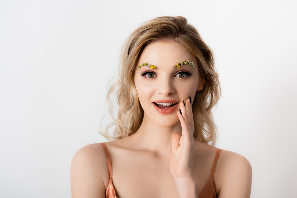 surprised beautiful blonde woman with wildflowers on eyebrows isolated on white - Photo, Image