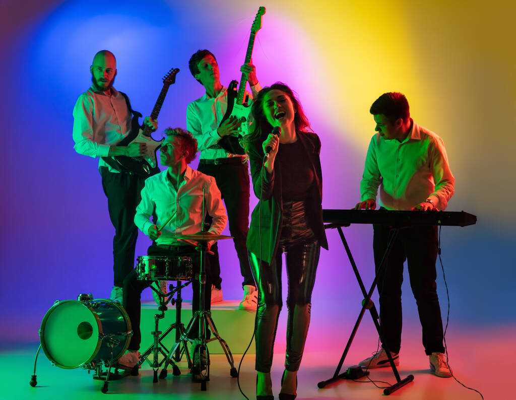 Giovani musicisti caucasici, banda che suona su sfondo sfumato in luce al neon. Concetto di musica, hobby, festival - Foto, immagini