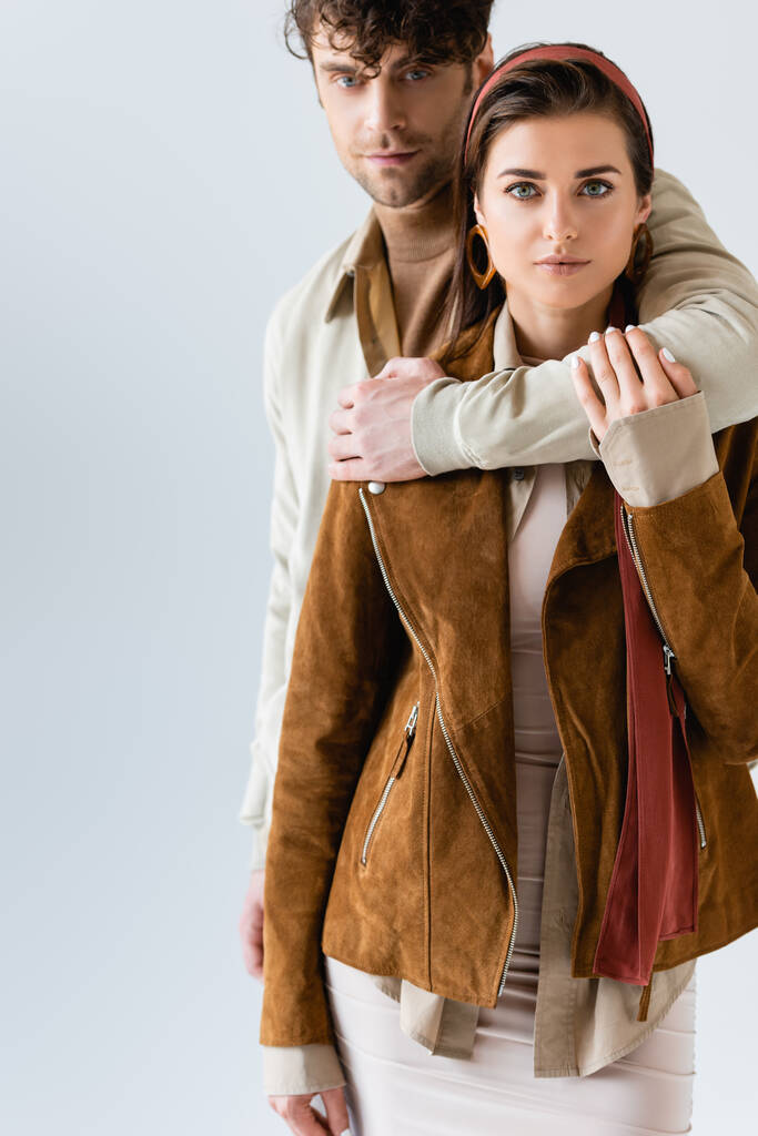 όμορφος άντρας αγκαλιάζει κομψή γυναίκα σε suede σακάκι απομονώνονται σε γκρι - Φωτογραφία, εικόνα