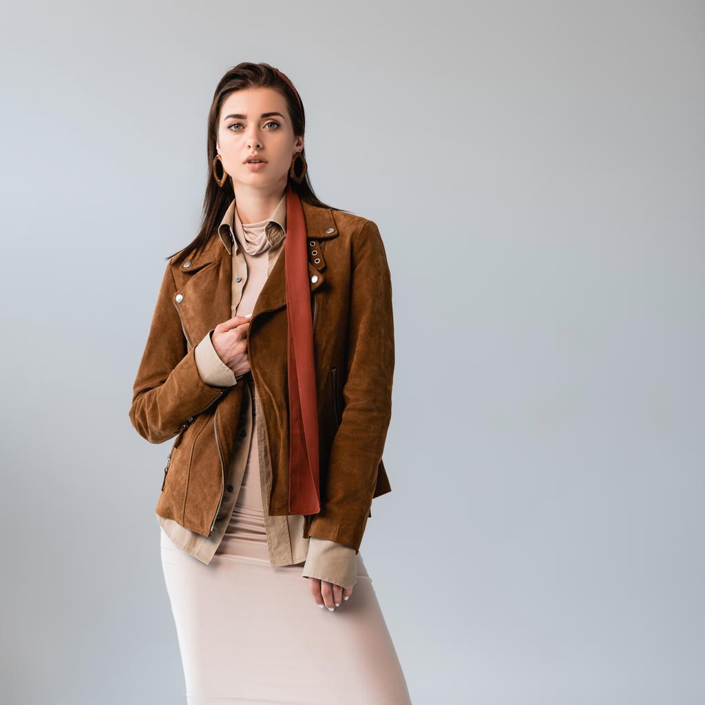 atraente, menina da moda tocando jaqueta de camurça enquanto olha para a câmera isolada no cinza
 - Foto, Imagem