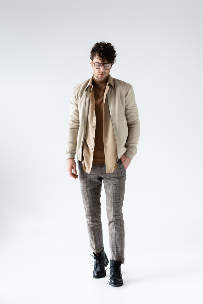 full length view of fashionable man in autumn clothes posing with hand in pocket on grey - Photo, Image