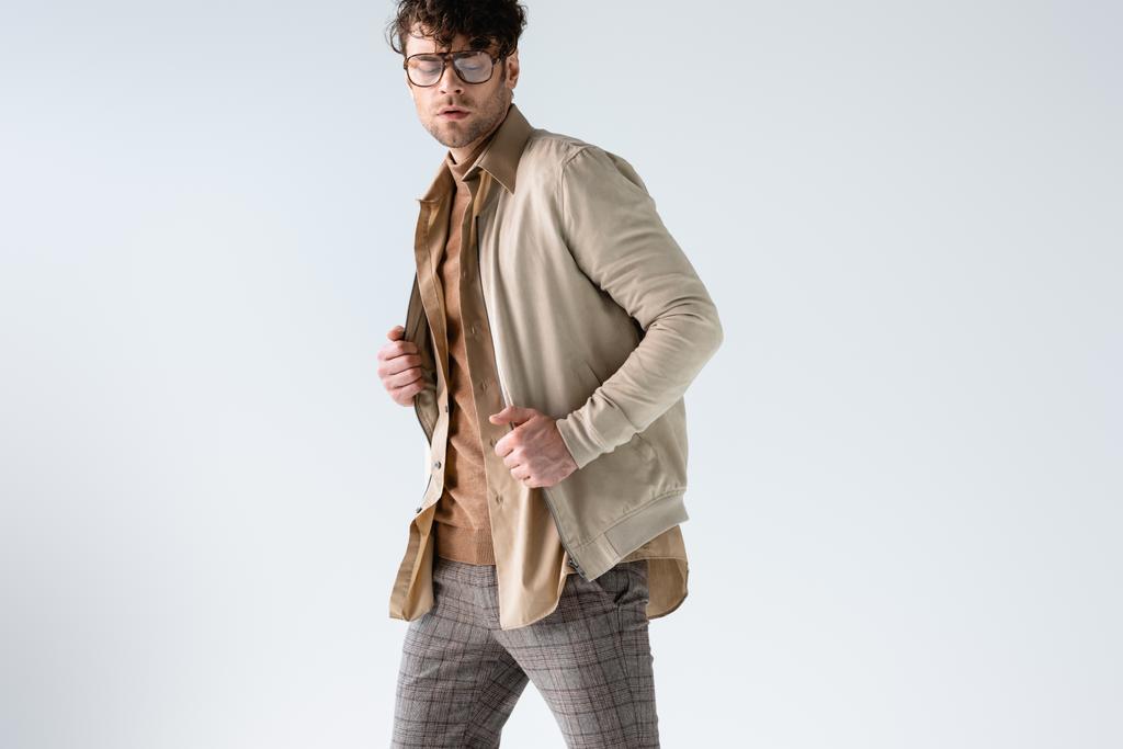 mooie, stijlvolle man aanraken jas terwijl poseren met gesloten ogen geïsoleerd op grijs - Foto, afbeelding
