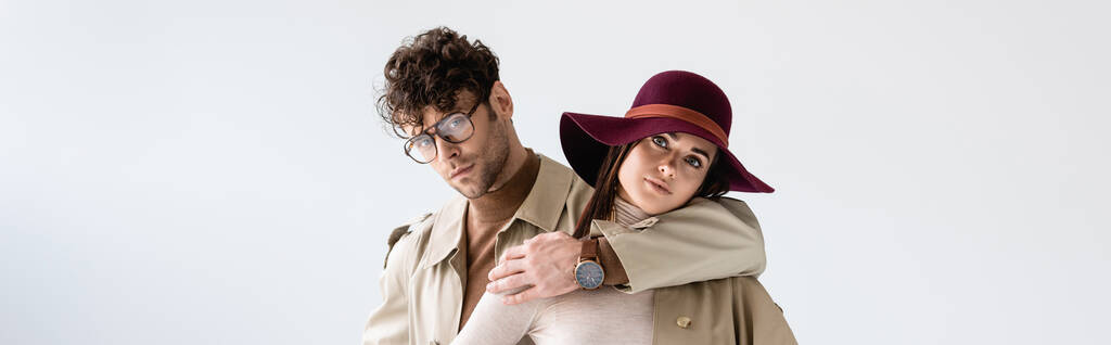 panoramic shot of handsome man hugging stylish woman in hat while looking at camera isolated on white - Photo, Image