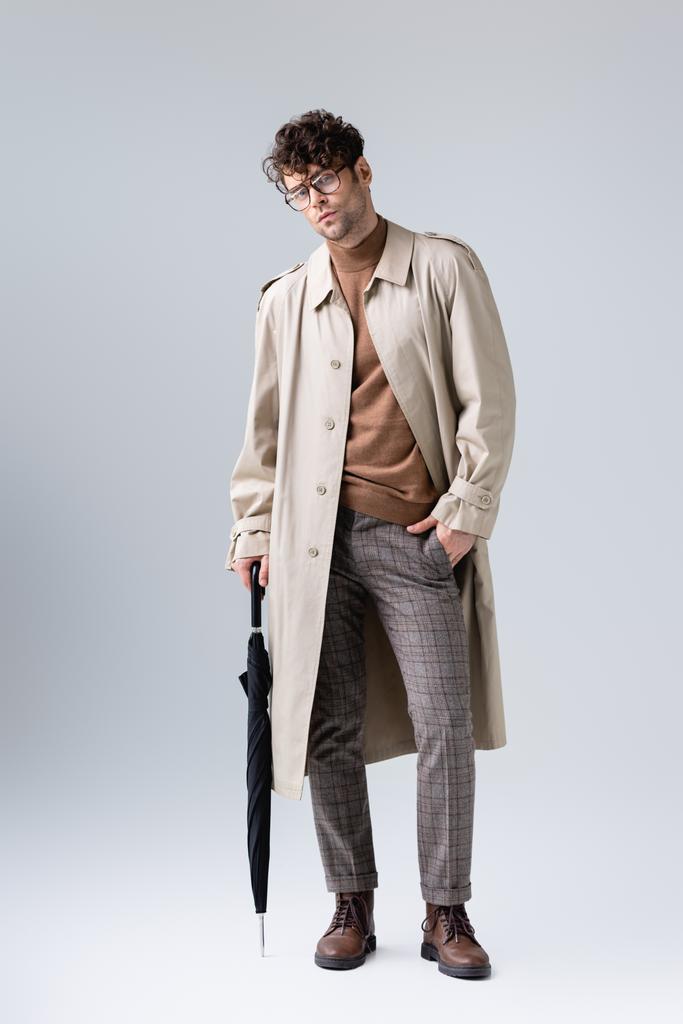 vista integrale dell'uomo elegante con ombrello piegato che tiene la mano in tasca sul grigio - Foto, immagini