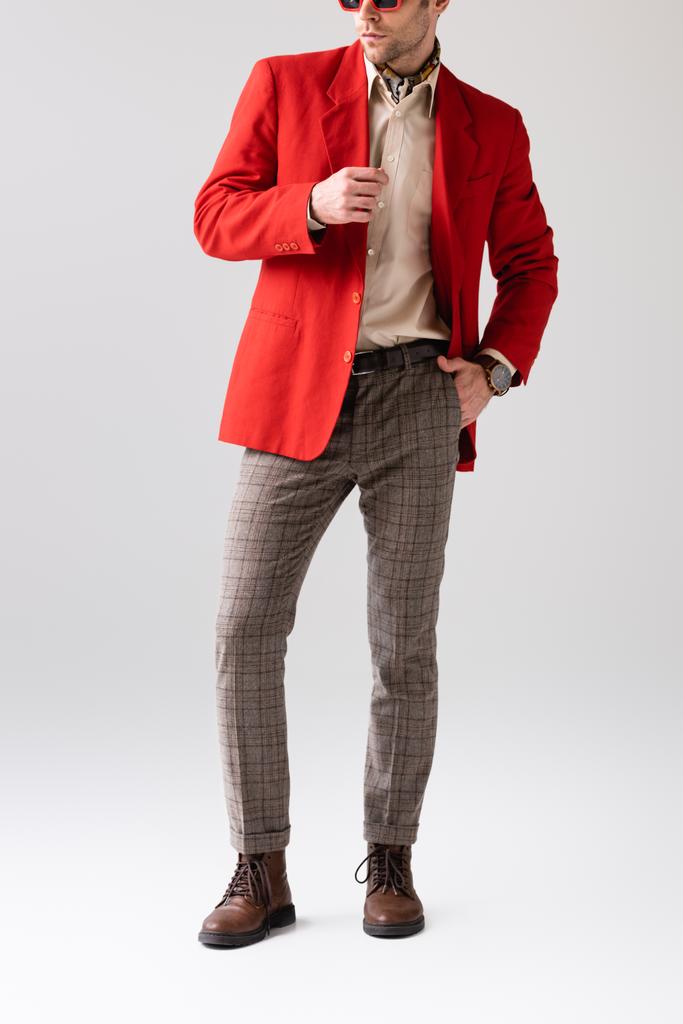 обрезанный вид стильного мужчины, держащегося за руку в кармане и касающегося красного блейзера на сером - Фото, изображение