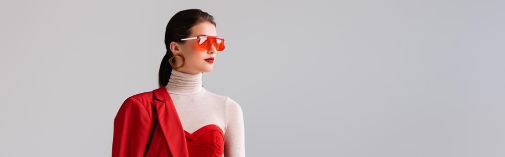 πανοραμική φωτογραφία του κομψό κορίτσι με κόκκινα γυαλιά ηλίου κοιτάζοντας μακριά απομονώνονται σε γκρι - Φωτογραφία, εικόνα